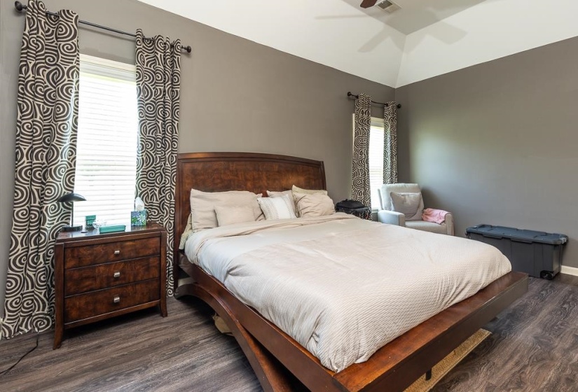 Bedroom featuring vaulted ceiling, wood-finish flooring, and two windows with blinds