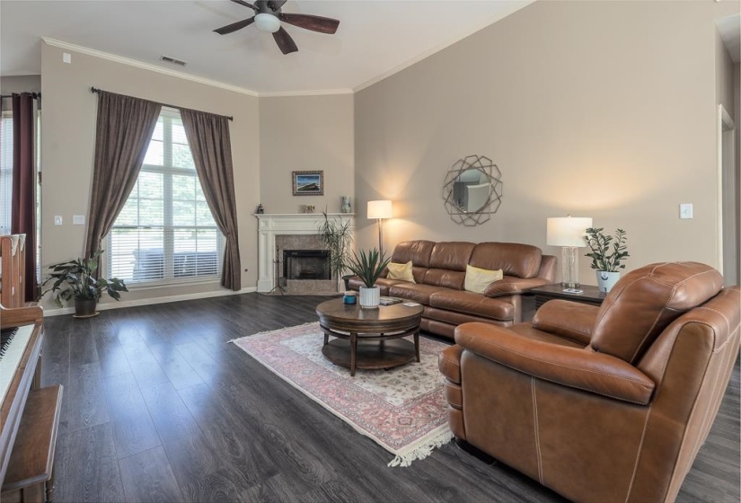 Living area featuring high ceilings, wood-finish flooring, a fireplace with a white mantel, and a large window with blinds