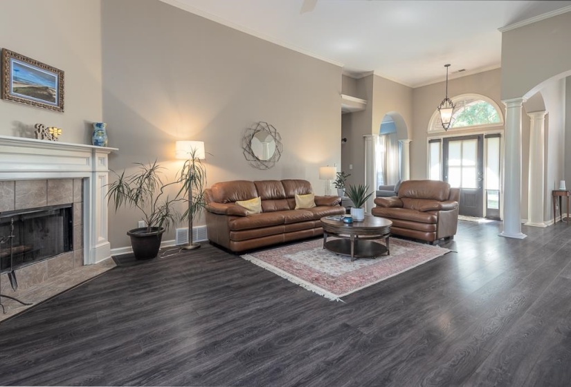 Living area featuring dark wood-finish flooring, a white mantel fireplace with tile surround, vaulted ceilings, and a light-filled entryway with an arched transom window and sidelights