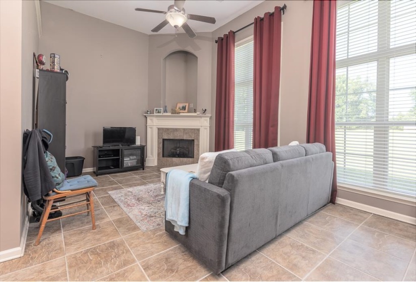 Spacious living area featuring vaulted ceilings, a tiled fireplace with a white mantel, and large windows with horizontal blinds