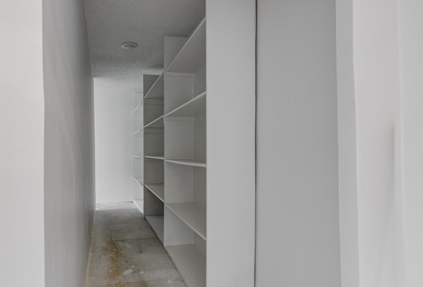 Built-in white shelving system providing ample storage within a narrow hall, featuring a recessed ceiling light