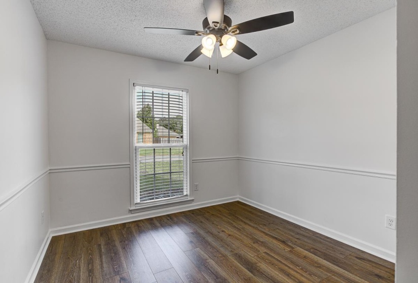 Room with wood-finish flooring, white walls with chair rail molding, and a window with blinds