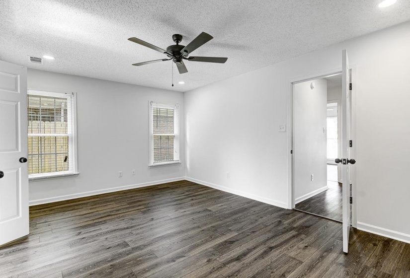 Spacious room featuring wood-finish flooring, two windows with blinds, a ceiling fan, and recessed lighting