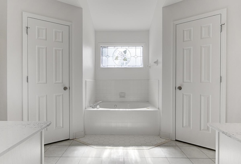 Built-in soaking tub with white subway tile surround, complemented by a decorative stained-glass window