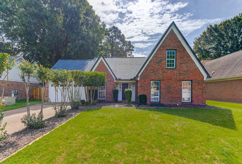 Brick facade residence with a prominent gabled roofline, featuring a manicured front lawn and mature landscaping