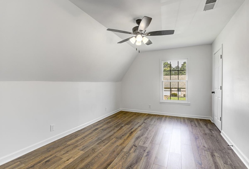 Room featuring wood-finish flooring, a ceiling fan with integrated lighting, a double-hung window with grid pattern, a white paneled door, and angled wall details