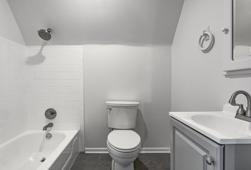 Bathroom featuring a full tub and shower with white subway tile surround, white vanity sink, chrome faucet, and dark flooring