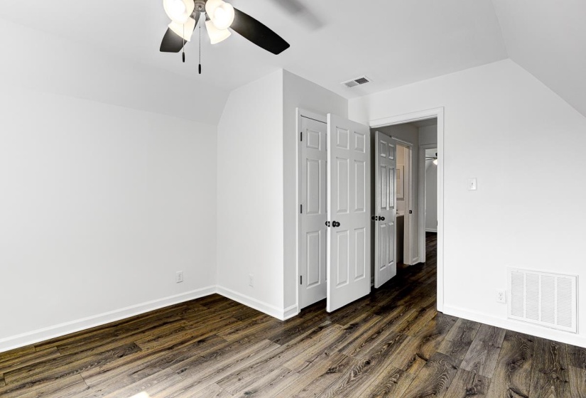 Spacious room featuring wood-finish flooring, crisp white walls, and a ceiling fan with light fixture