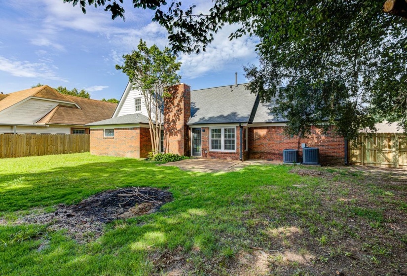 Expansive backyard with a brick and siding exterior, a large patio area, and mature trees providing natural shade