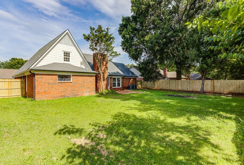 Spacious backyard featuring a manicured lawn, brick and white siding exterior, and a newly installed privacy fence
