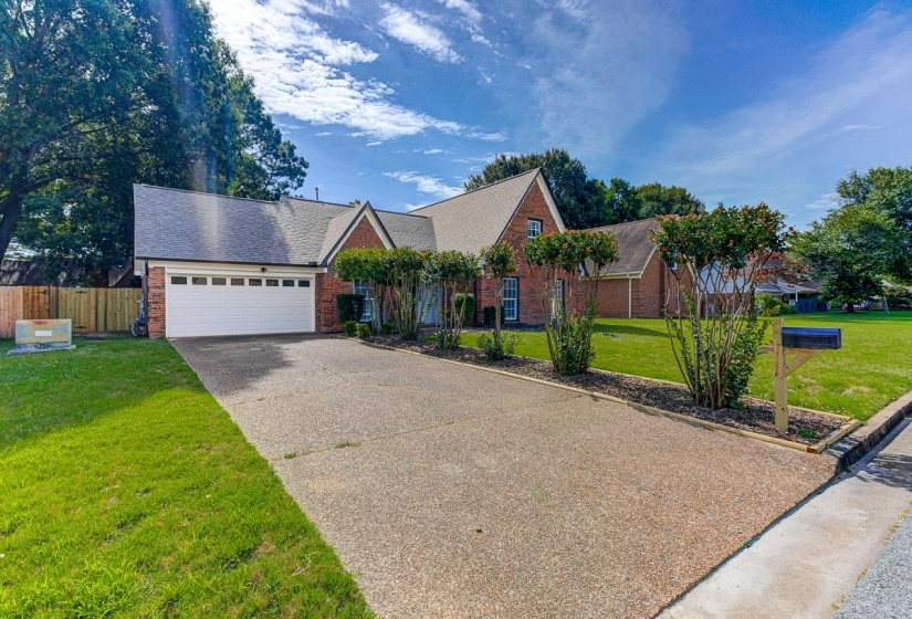 Brick residence featuring an attached two-car garage with a white door, a concrete driveway, mature landscaping, and a manicured lawn