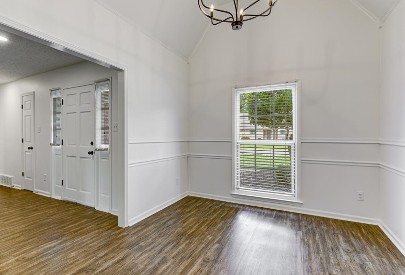 Room featuring wood-finish flooring, white walls with wainscoting, and a vaulted ceiling with a modern chandelier