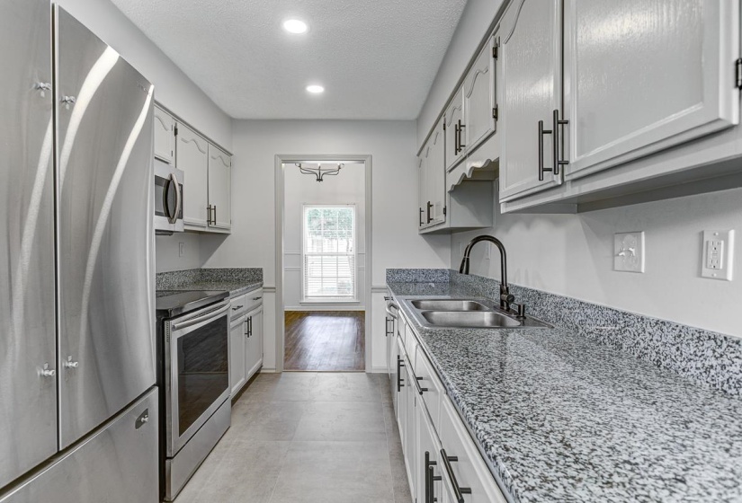 Galley kitchen featuring light gray cabinetry with black hardware, granite-style countertops, and stainless-steel appliances