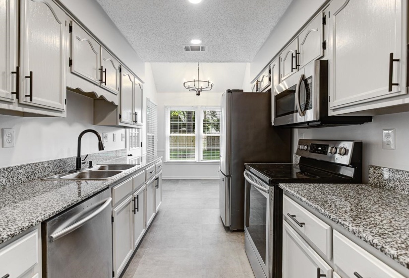 Galley kitchen featuring white cabinetry with black hardware, granite countertops, stainless steel appliances, and tile flooring