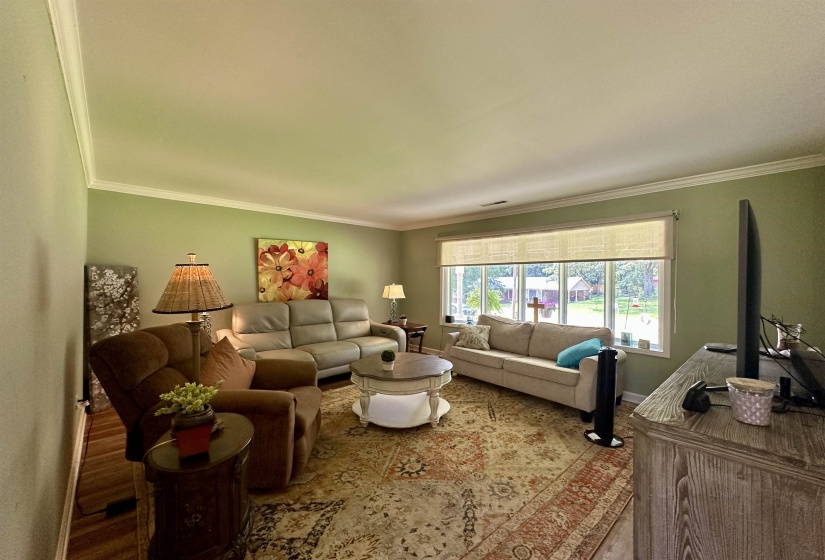 Spacious living area featuring crown molding, neutral wall color, and wood-finish flooring