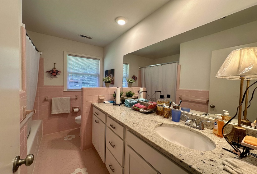Bathroom featuring a built-in bathtub, a window with blinds, a vanity with a drop-in sink, and a large wall mirror