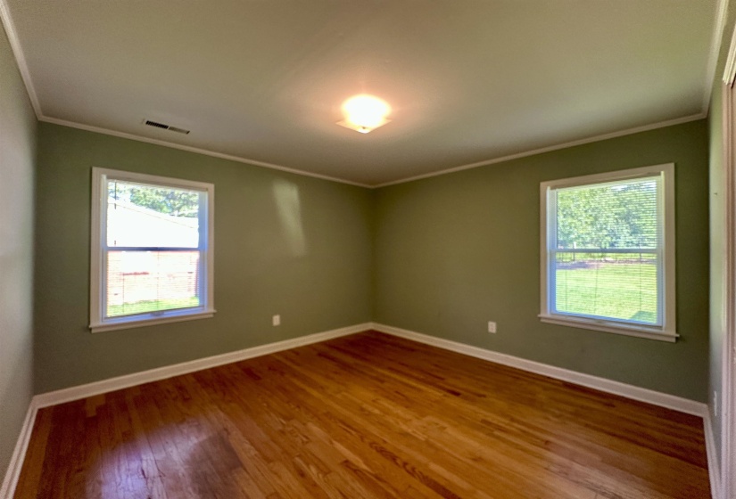 Interior room featuring wood-finish flooring, two windows with blinds, a ceiling-mounted light fixture, and crown molding