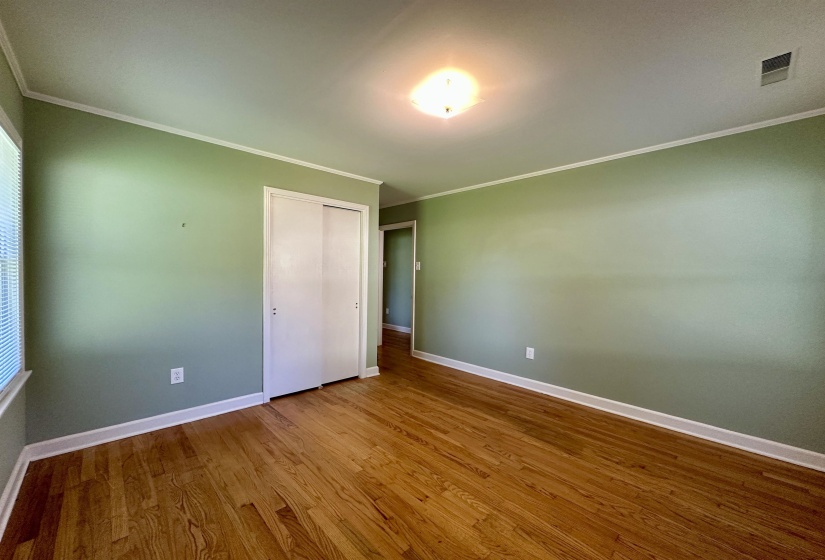 Interior room featuring wood-finish flooring, light green walls, white baseboards, and crown molding