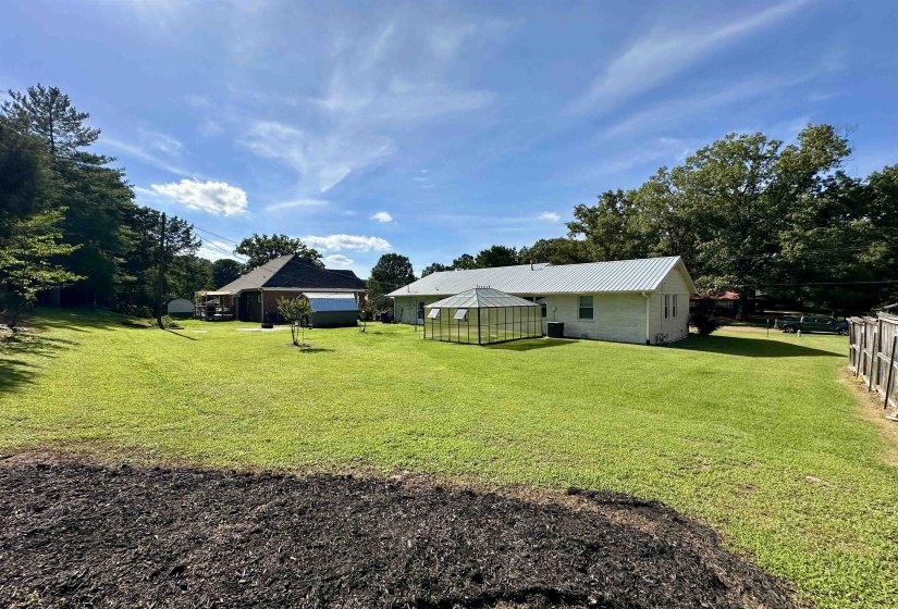 Expansive backyard featuring a manicured lawn, a detached building with a covered patio, a separate structure with a metal roof, and a visible fence line