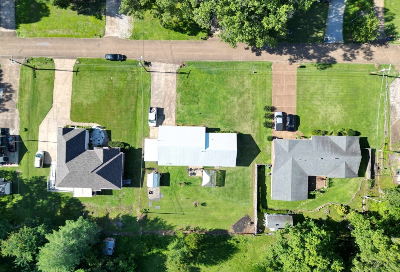 Aerial perspective showcasing a property with a gray shingle roof, a paved driveway, and a spacious green lawn