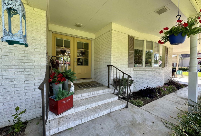 Welcoming front entry with white brick facade, double glass-paneled entry doors, a curved bay window, and a covered porch