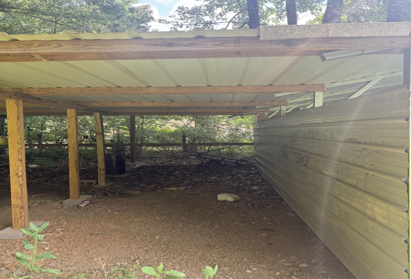 Carport structure with a corrugated metal roof, wood framing, and a gravel floor