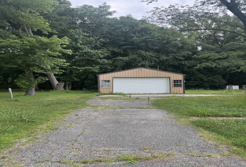 Detached garage structure featuring a tan metal exterior, white garage door, and two window units