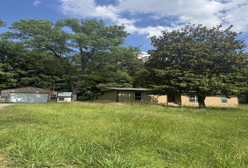 Expansive grassy lot featuring two detached structures, mature trees, and a gravel driveway