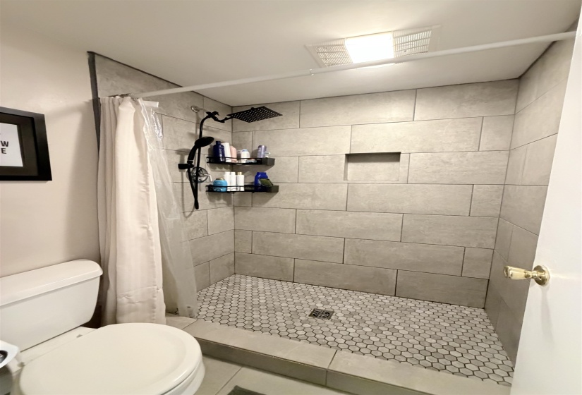 Shower featuring large-format wall tiling, hexagonal floor tiling, waterfall showerhead