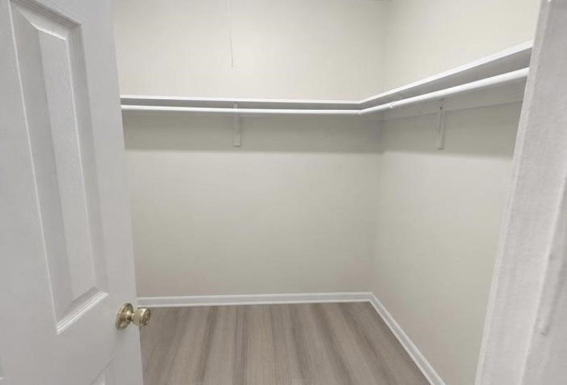 Large L shape Walk-in closet featuring wood-finish flooring, white baseboards, and built-in shelving with hanging rods