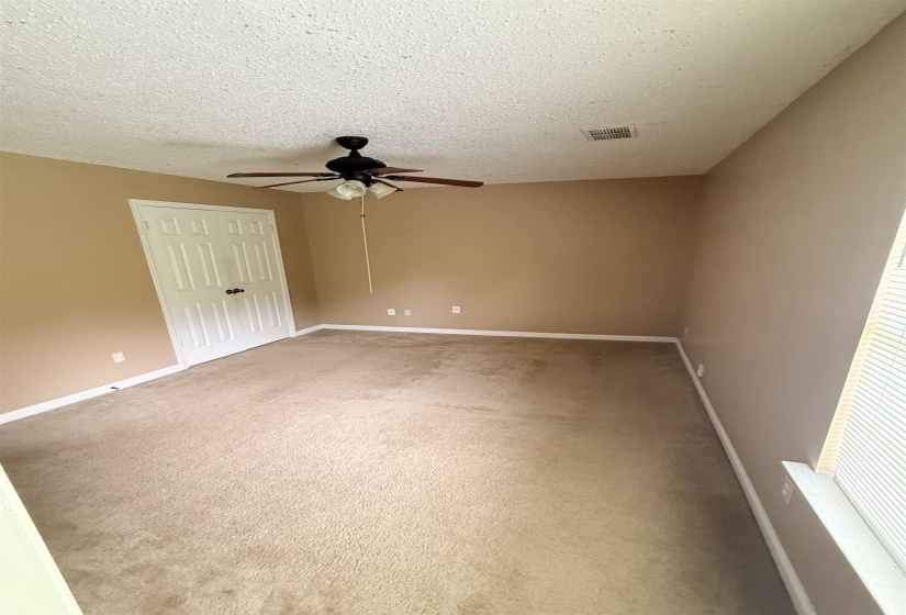 Carpeted room featuring neutral wall paint, a white paneled door with black hardware, white baseboards, and a ceiling fan with integrated lighting