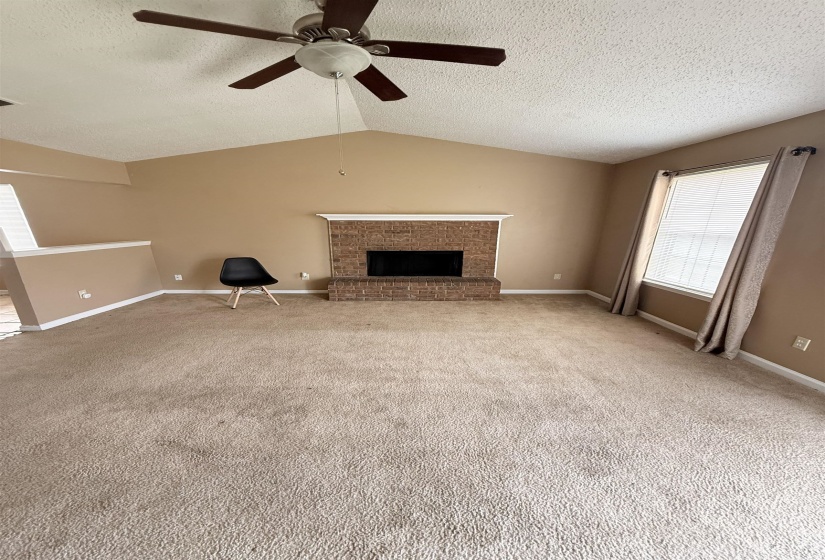 Spacious living area featuring a vaulted ceiling and a ceiling fan with integrated lighting