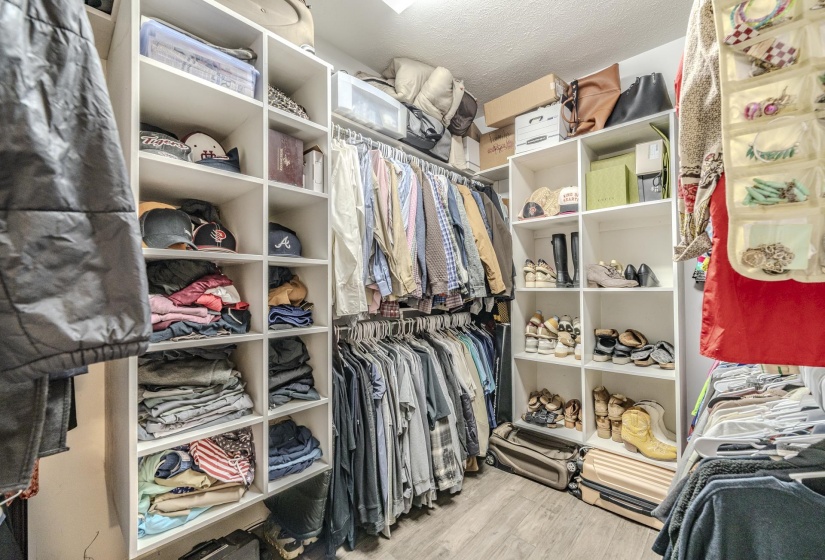 Walk-in closet featuring built-in white shelving, multiple hanging rods, and wood-finish flooring