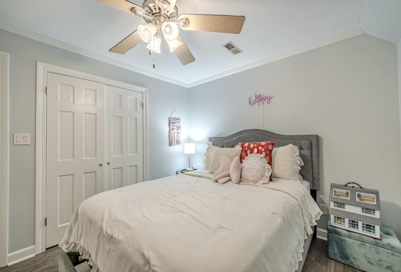 Bedroom featuring crown molding, neutral wall color, wood-finish flooring, a built-in closet with paneled bifold doors, and a ceiling fan with integrated lighting