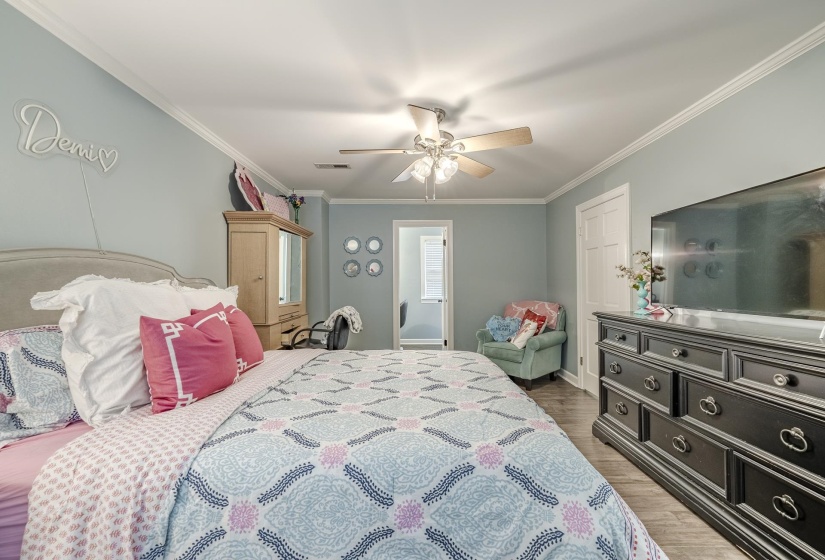 Spacious room featuring light blue walls, crown molding, a ceiling fan with integrated lighting, wood-finish flooring, and a white paneled door