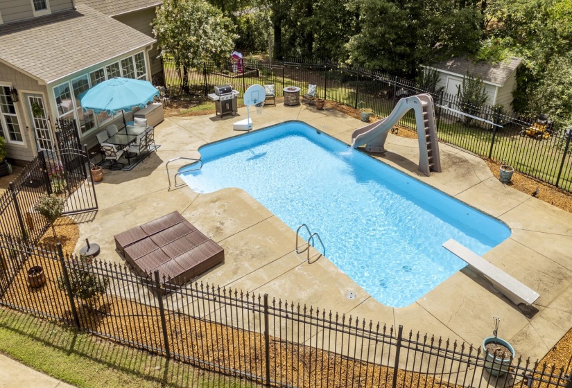 Expansive outdoor area featuring a freeform swimming pool with a slide and diving board, surrounded by a concrete patio and black wrought iron fencing