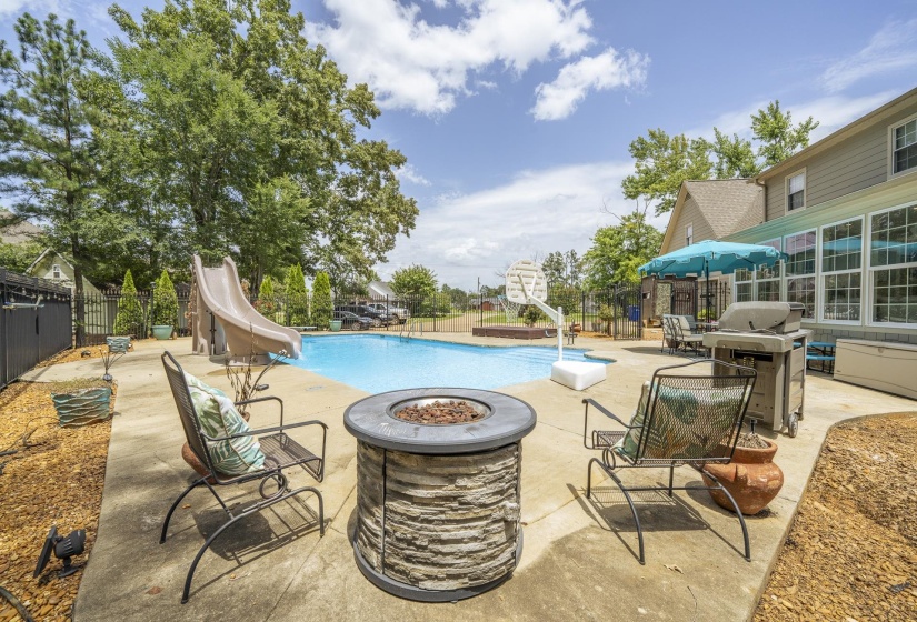 Concrete patio featuring a stacked stone fire pit and an in-ground swimming pool with an attached slide
