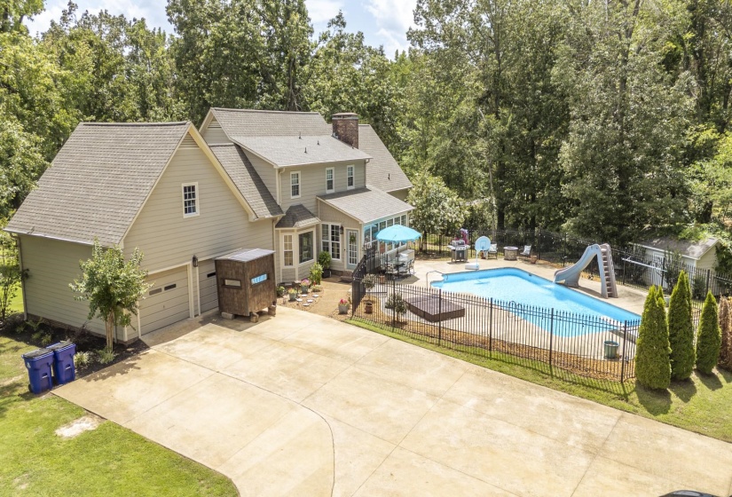 Expansive concrete driveway leading to a residence featuring a two-car garage, a fenced in-ground swimming pool, and a dedicated pool deck