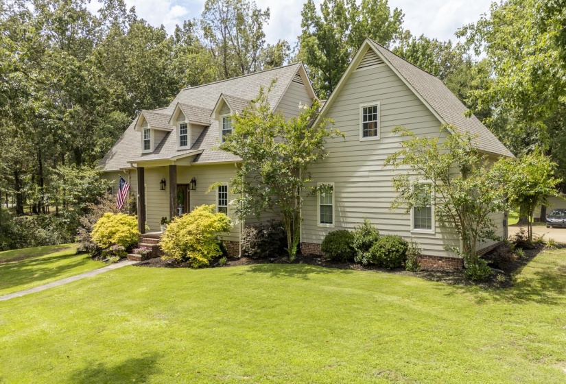 Spacious exterior with light-colored siding, a prominent front porch with pillars, multiple dormer windows, a pitched roofline, and established landscaping