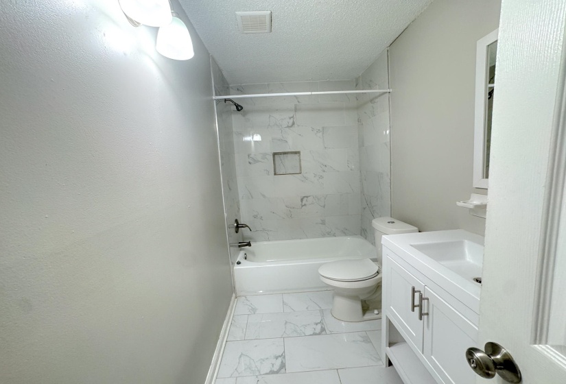 Bathroom featuring a white vanity with dual doors and open shelving, a white toilet, and a white bathtub with a tile surround