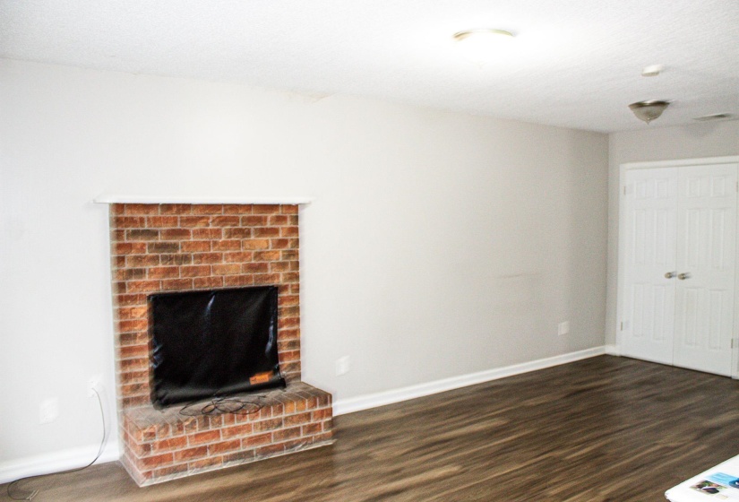 Brick fireplace with white mantel and hearth, wood-finish flooring, light grey painted walls, white baseboards, and double white closet doors