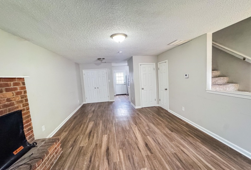 Spacious living area featuring wood-finish flooring, light gray walls, a brick fireplace, and white trim