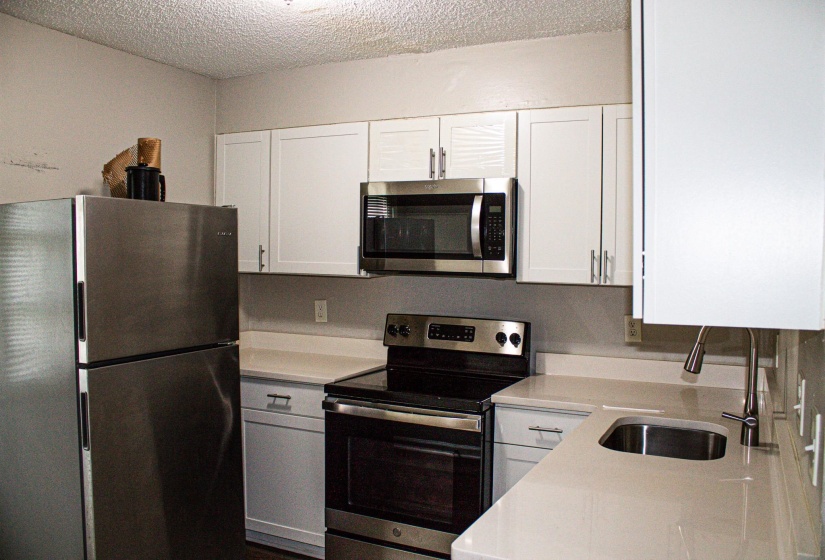 Kitchen featuring white cabinetry, stainless steel appliances, light-toned countertops, and an undermount sink with a gooseneck faucet