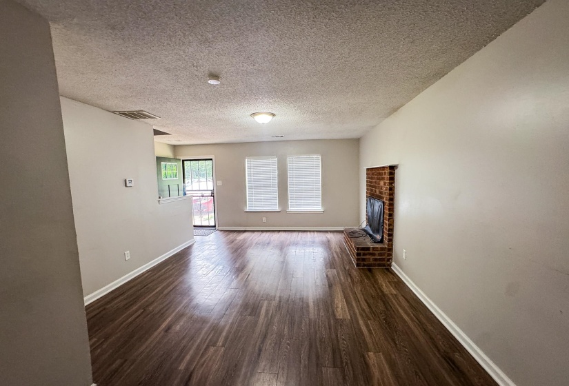 Spacious living area featuring wood-finish flooring, light neutral wall paint, and a brick-detailed hearth