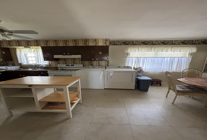 Kitchen with white electric stove, a ceiling fan, washing machine and dryer, light countertops, and light tile patterned floors