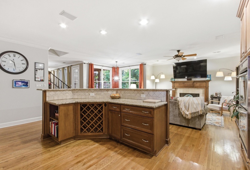 Open-concept living space featuring wood-finish flooring, a kitchen island with built-in wine storage, a tiled backsplash, and stone countertops