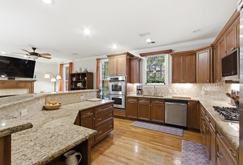 Open-concept kitchen featuring extensive granite countertops, wood-finish flooring, stainless steel appliances, and wood cabinetry with under-cabinet lighting