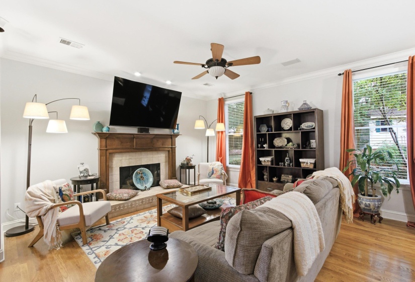 Living area featuring wood-finish flooring, a fireplace with a wood mantle and tile surround, and multiple windows with blinds