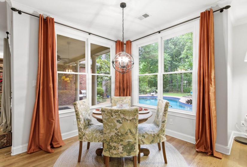 Corner dining area featuring large windows overlooking a backyard pool and mature trees