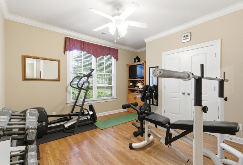 Hardwood flooring in a versatile room featuring a ceiling fan, crown molding, double windows with blinds, and white double-door closet